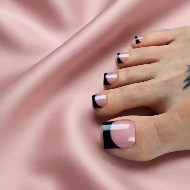 Glossy black toe tips on a sheer pink base resting on blush pink silk.