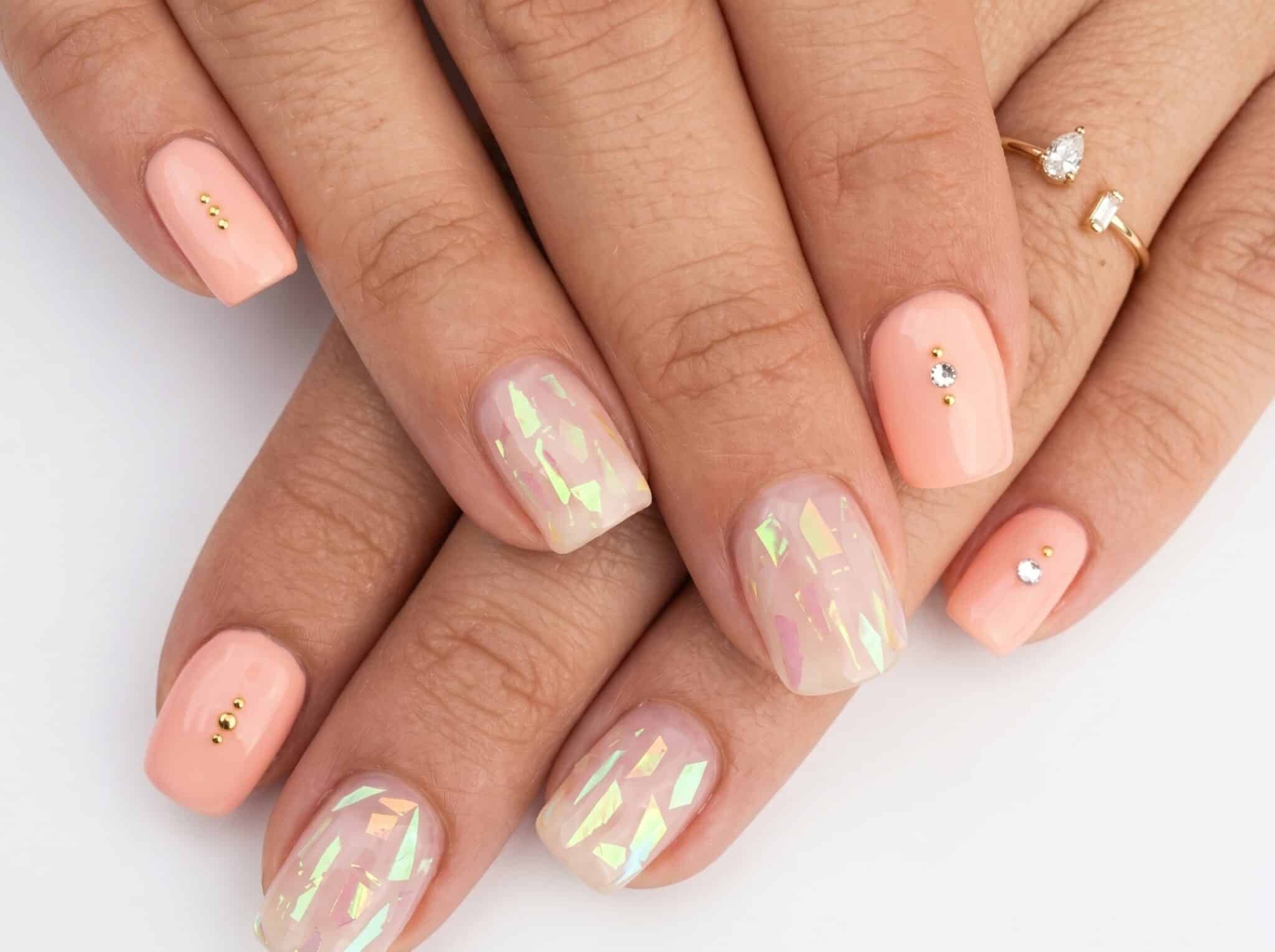 Glossy nude nails with a soft pearly chrome finish and tiny gold accents